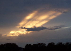 Photo of broad streaks of yellow sunlight across evening clouds